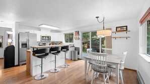 Una cucina moderna con mobili bianchi, un frigorifero in acciaio inossidabile e un'area pranzo con tavolo e sedie bianche.