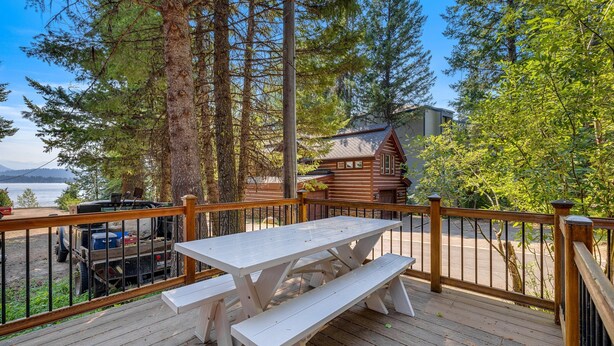 Un terrazzo in legno con tavolo da picnic e panche, immerso tra alberi alti e un rifugio di montagna.