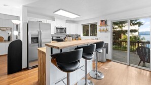 Una cucina moderna con un’area con sgabelli in legno, un frigorifero in acciaio inossidabile e vista all’esterno tramite una porta scorrevole in vetro.
