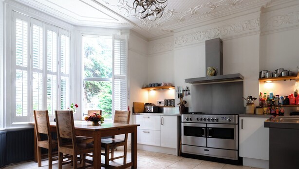A kitchen with a large stove, white cabinetry, and a dining area with wooden chairs and a table. - EBS London Stay (London)