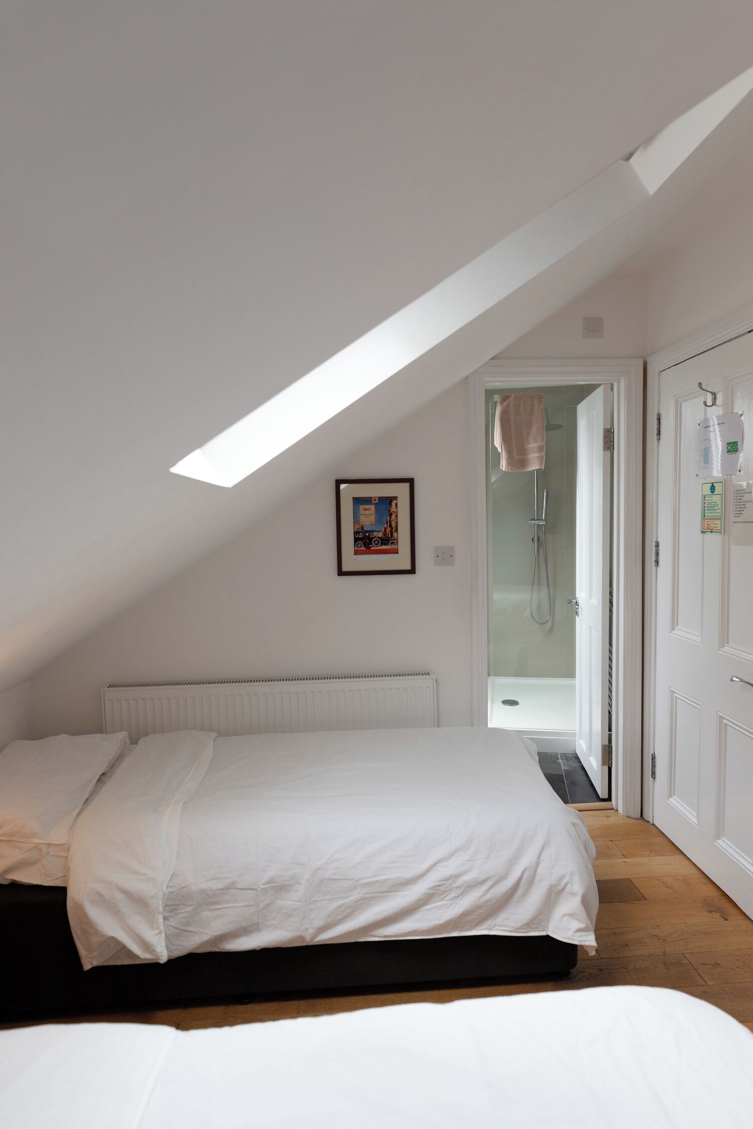 Un dormitorio con tragaluz, cama, radiador y zona de ducha.