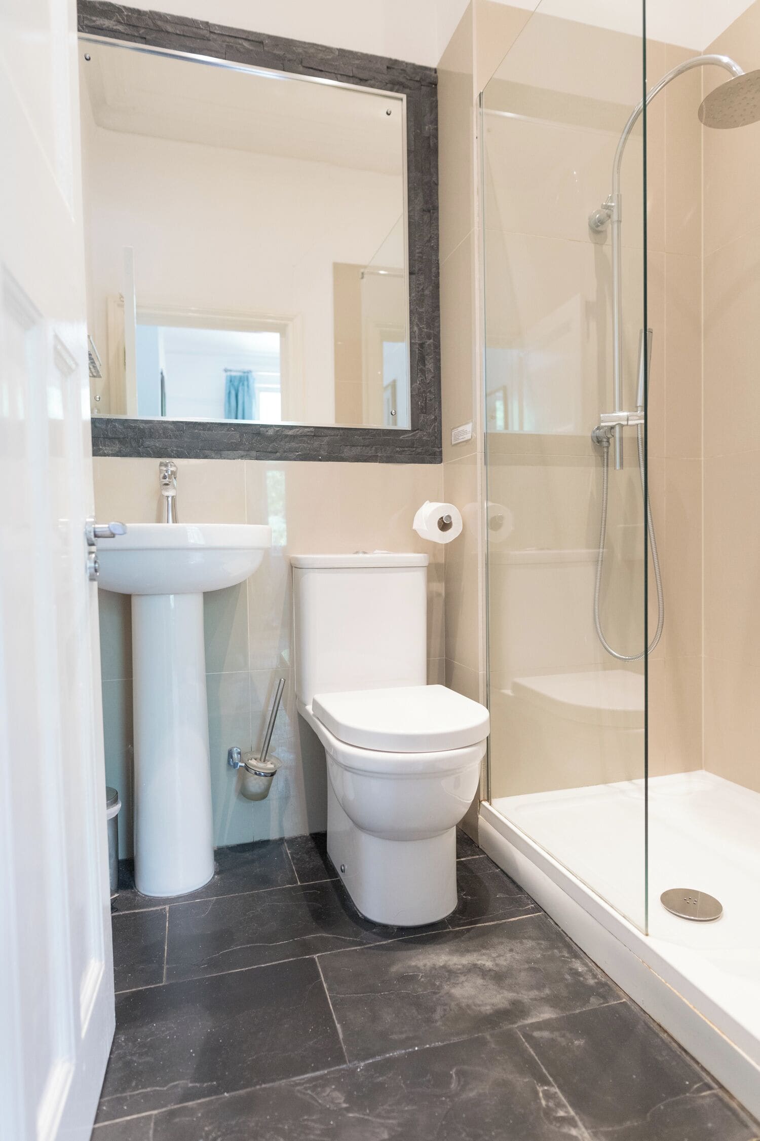 Un baño moderno con ducha envuelta en vidrio, lavamanos pedestal y retrete.