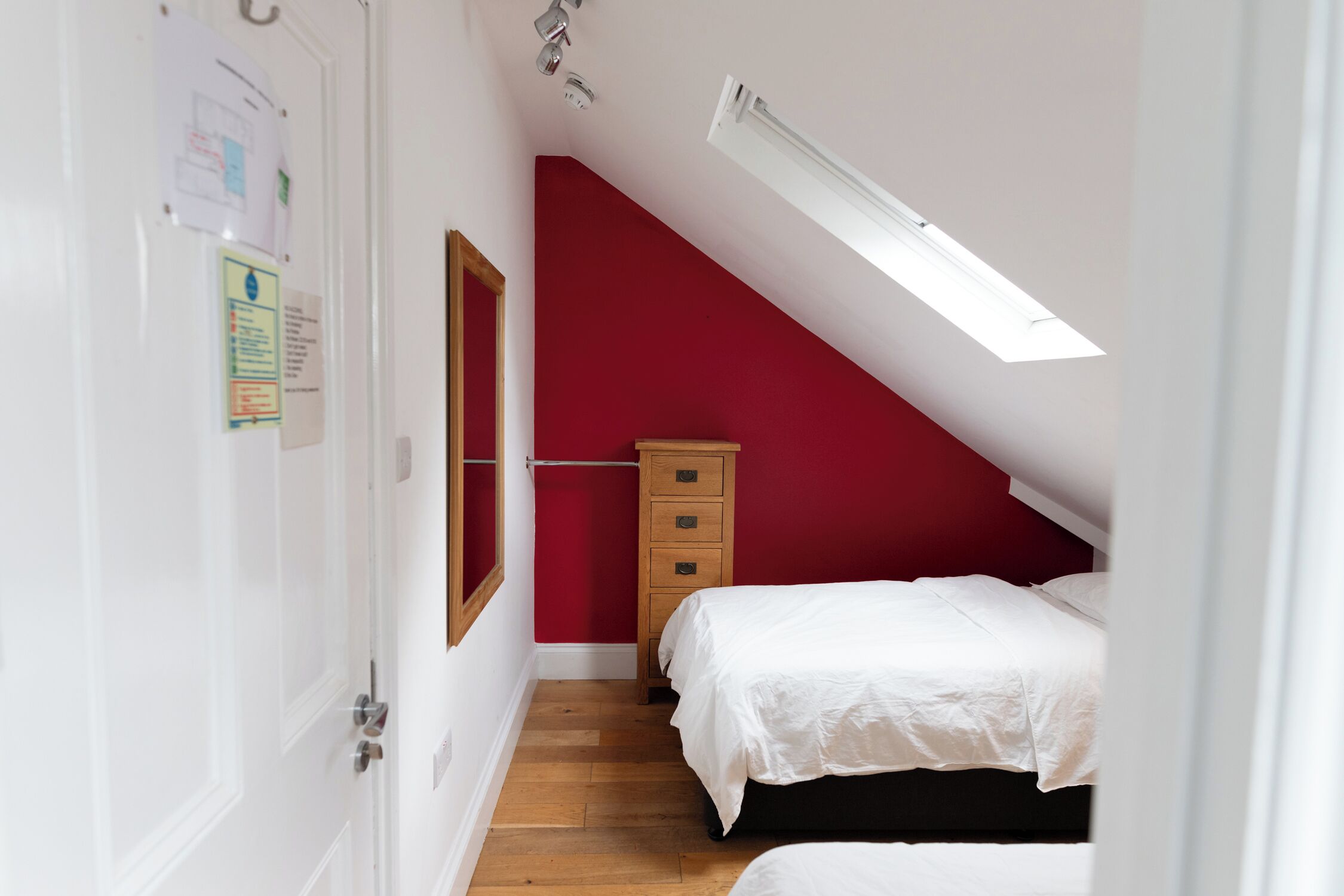 Une chambre avec un plafond en pente, une commode en bois et deux lits avec du linge de lit blanc.