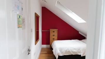 Une chambre avec un plafond en pente, une commode en bois et deux lits avec du linge de lit blanc.