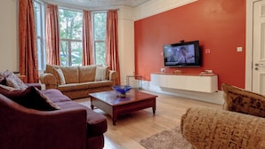 A living room with a sofa, a coffee table, and a television on a wall. - EBS London Stay (London)