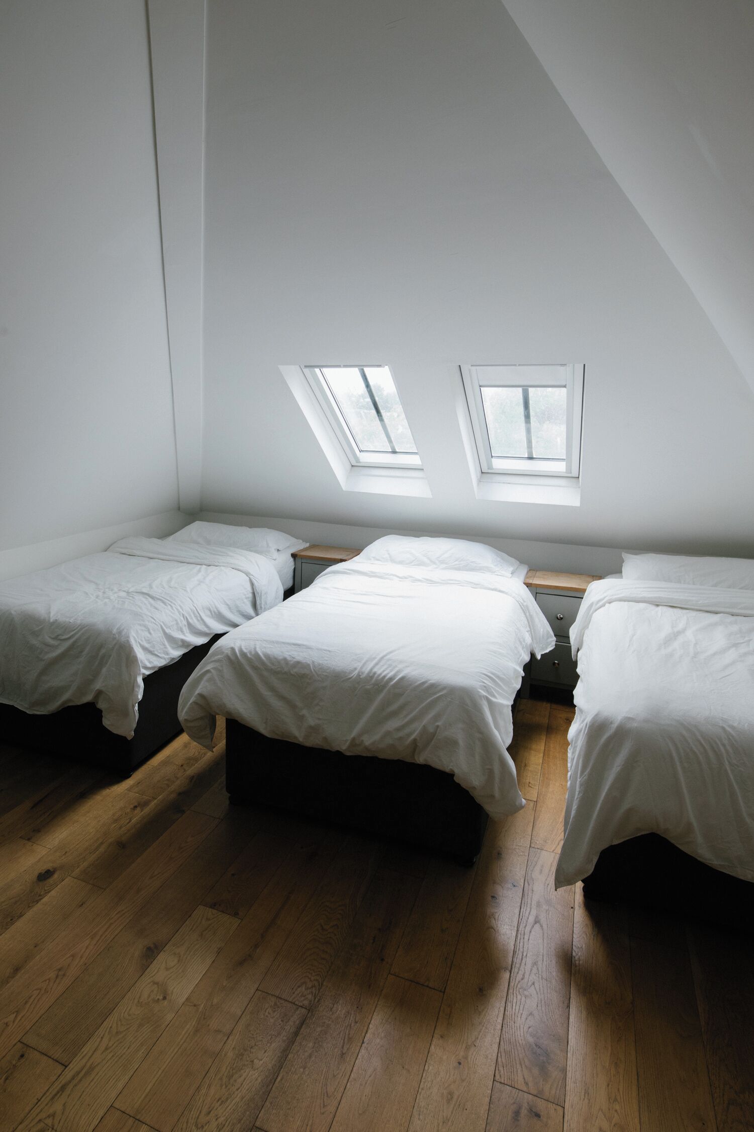 A room with three single beds, wooden flooring, and skylights.