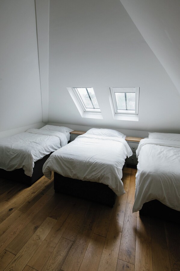 A room with three single beds, wooden flooring, and skylights.