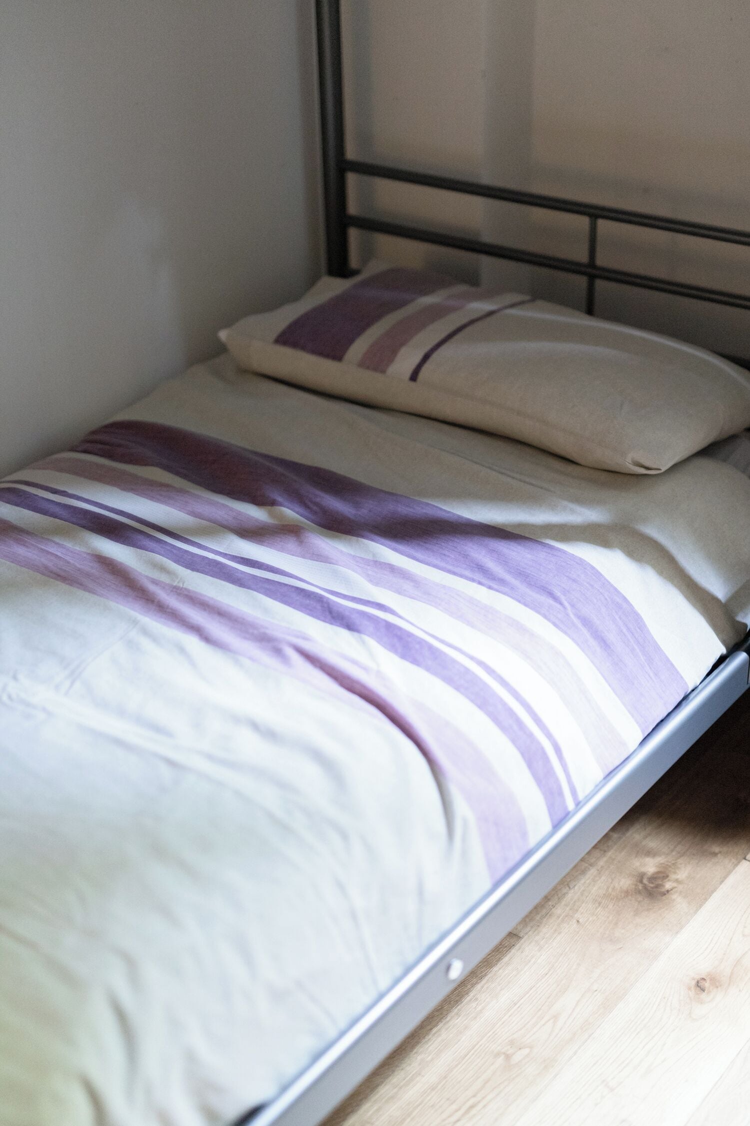 Un lit simple avec un cadre en métal, une couvre-lit rayée blanche et violette et un oreiller beige.