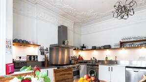 A modern kitchen with white cabinetry, stainless steel appliances, and a wooden dining table with a fruit bowl. - EBS London Stay (London)