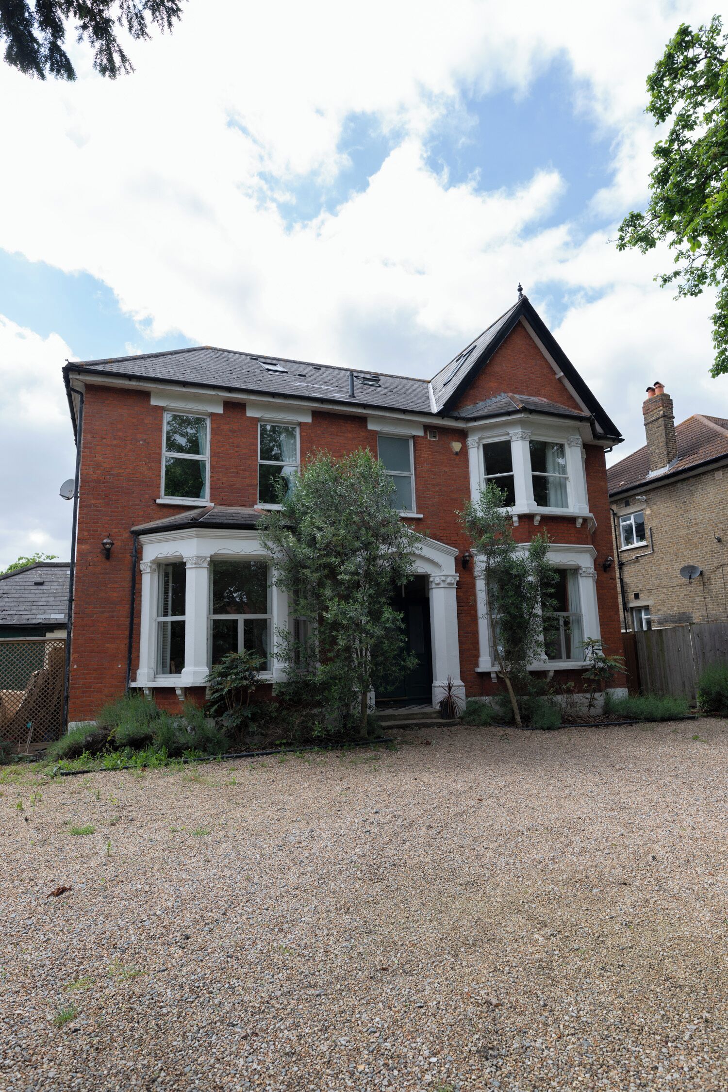 A two-story brick house with a gravel driveway and a small garden.