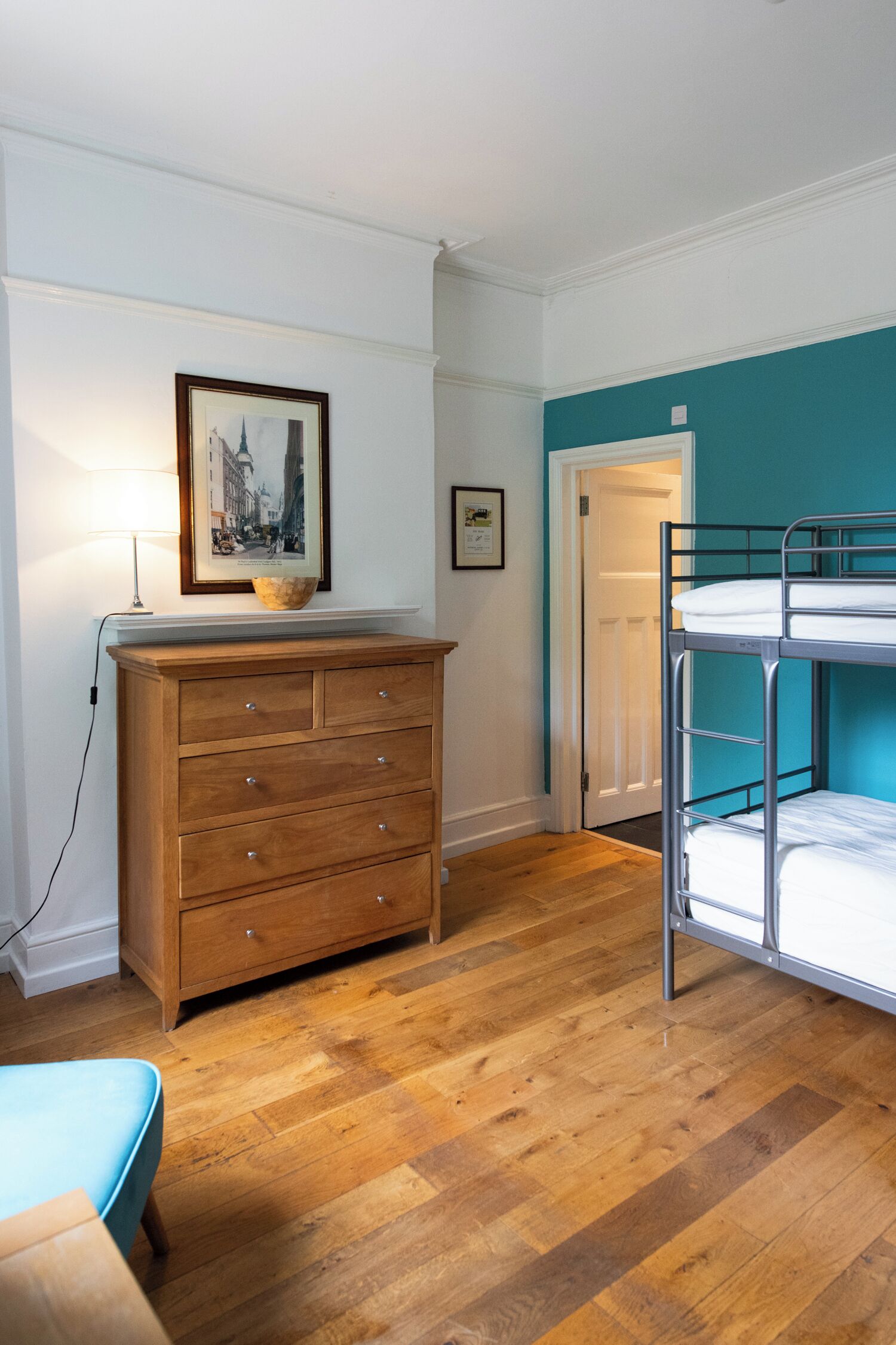 Una habitación con un aparador de madera, una cama litera, un cuadro enmarcado en la pared y una puerta.
