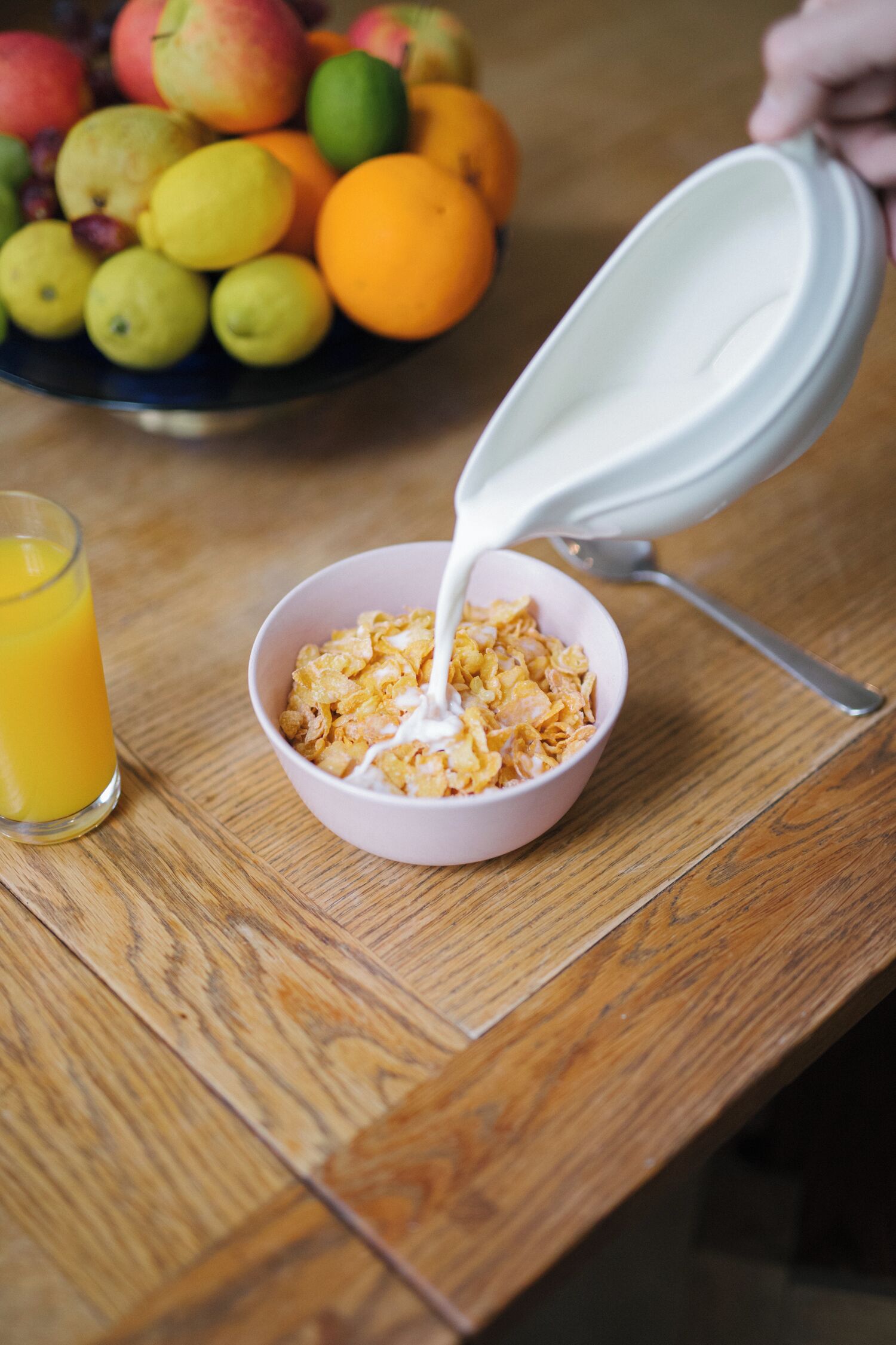 Un bol de céréales dans lequel on verse du lait, un verre de jus d’orange et, au fond, un autre bol rempli de fruits.