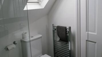 Un baño pequeño con tragaluz, inodoro, toallero y cabina de ducha con mampara de vidrio.