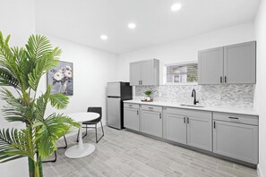 Eine moderne Küche mit grauen Schränken, einer weißen Arbeitsplatte und einem schwarzen Kühlschrank.