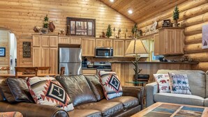 A cabin interior with a wooden interior, leather sofa, and a dining area. - Two Bears Cabin (Cabin 162) (Eagar)