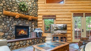 A log cabin interior with a stone fireplace, a television, and a cozy seating area. - Two Bears Cabin (Cabin 162) (Eagar)