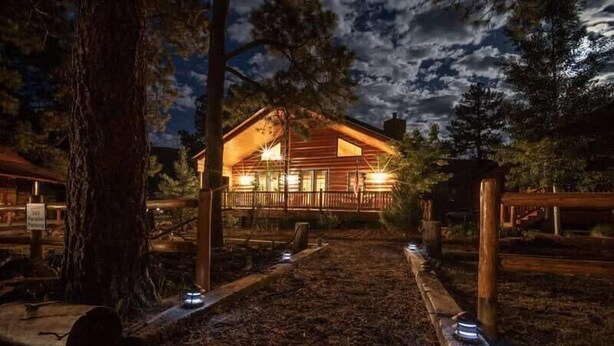 A wooden cabin with a porch, surrounded by trees and a clear sky. - Two Bears Cabin (Cabin 162) (Eagar)