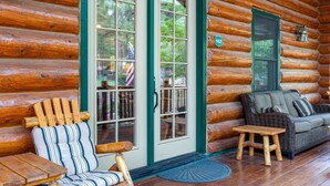 A log cabin with a wooden exterior, a sliding glass door, a wicker sofa, and a striped chair. - Two Bears Cabin (Cabin 162) (Eagar)