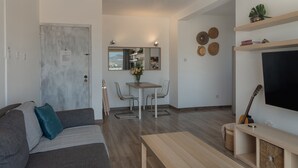 A modern living room with a sofa, a coffee table, a dining area with chairs, a TV, and a guitar. - Phaedrus Living Nicosia Heartside Flat  (Strovolos)