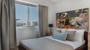 A modern bedroom with a large bed, a city view, and a colorful abstract painting. - Phaedrus Living Nicosia Heartside Flat  (Strovolos)