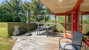 Een terras buiten met een tafel en stoelen, omgeven door een houten terras en een groene hek.