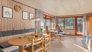 Een gezellige kamer met een houten eettafel, stoelen, een bank en een raam met gordijnen.