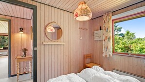 Een slaapkamer met een houten plafond, een bed met wit beddengoed, een ronde spiegel, een hanglamp en een raam met gordijnen.