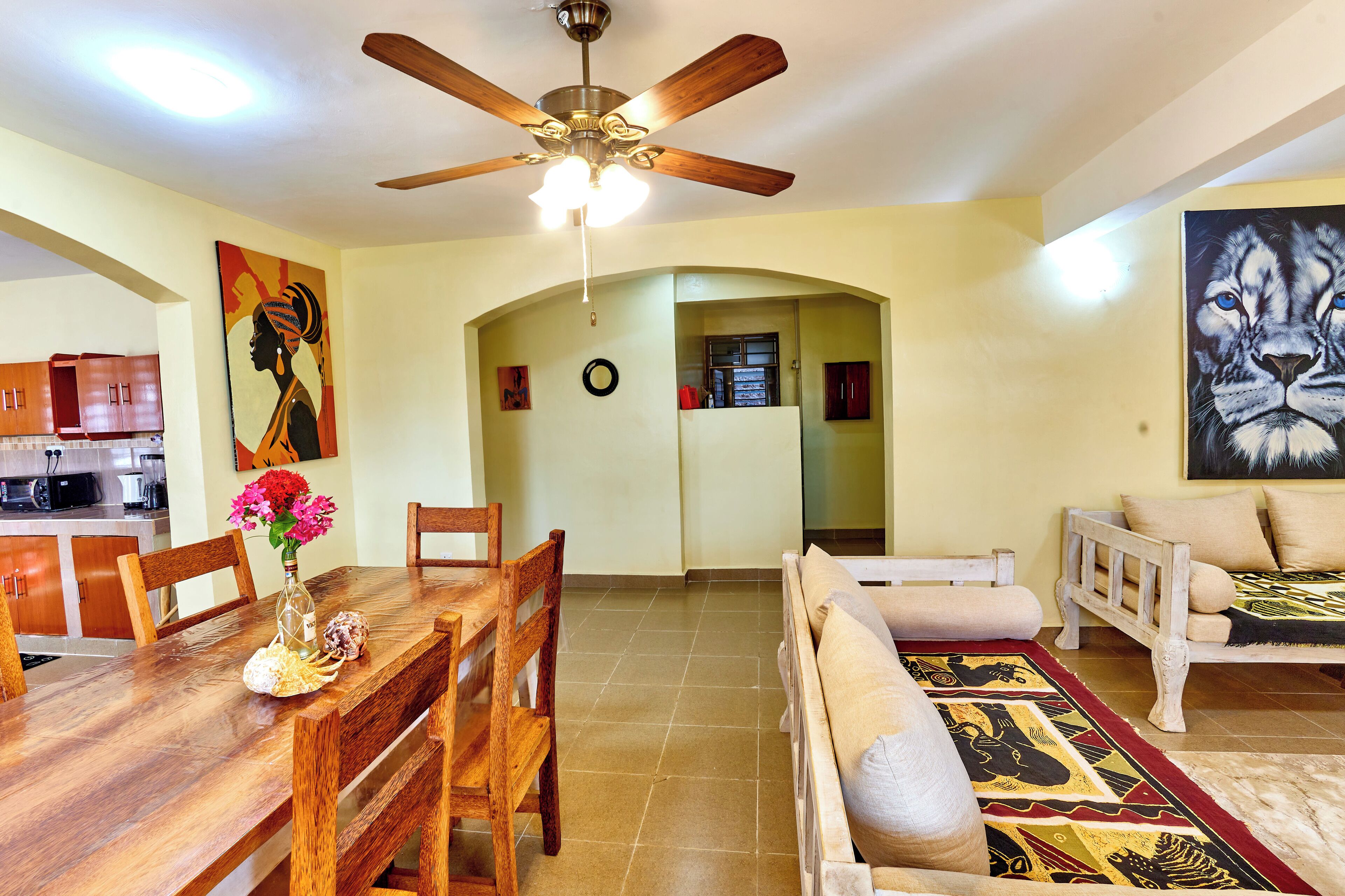 A spacious living area with a wooden dining table, a sofa, and a ceiling fan.