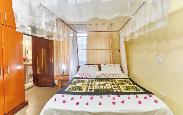 A bedroom with a bed, a wooden wardrobe, a nightstand, and a window with curtains. - DIANI BEACH GOLD APARTMENTS  (Diani Beach)