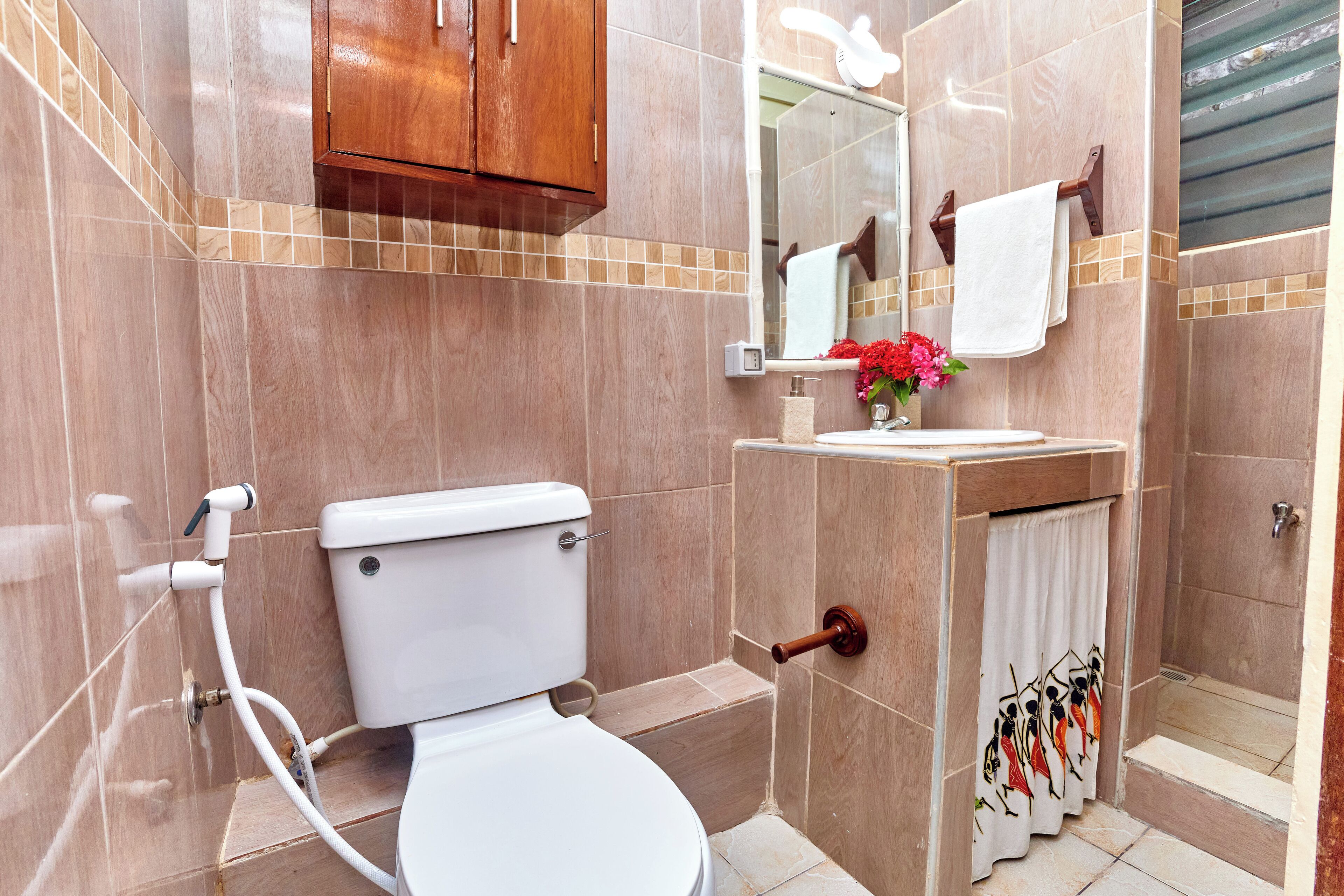 A bathroom with a toilet, sink, shower, and a wooden cabinet.