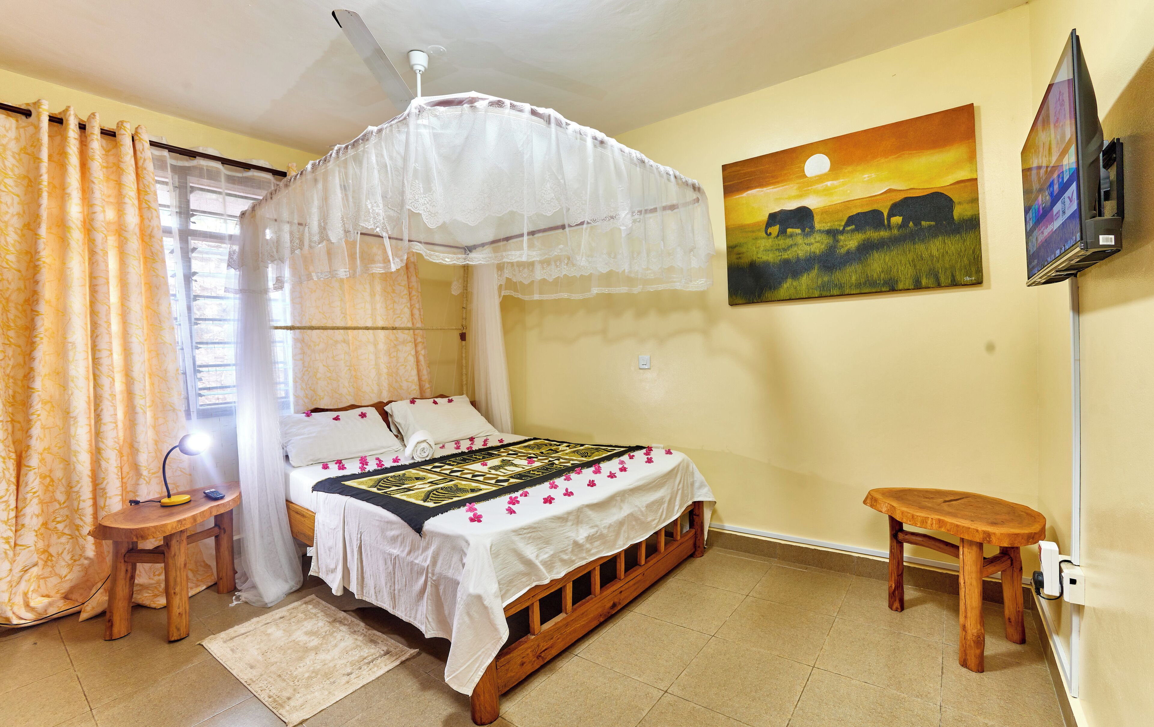 A room with a bed, a bedside table, a nightstand, a TV, and a painting on the wall.