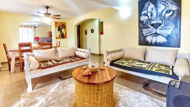 A living room with a sofa, a coffee table, and a painting of a lion's face on the wall. - DIANI BEACH GOLD APARTMENTS  (Diani Beach)