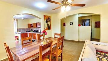 A dining area with a wooden table and chairs, a ceiling fan, and a kitchen in the background.
