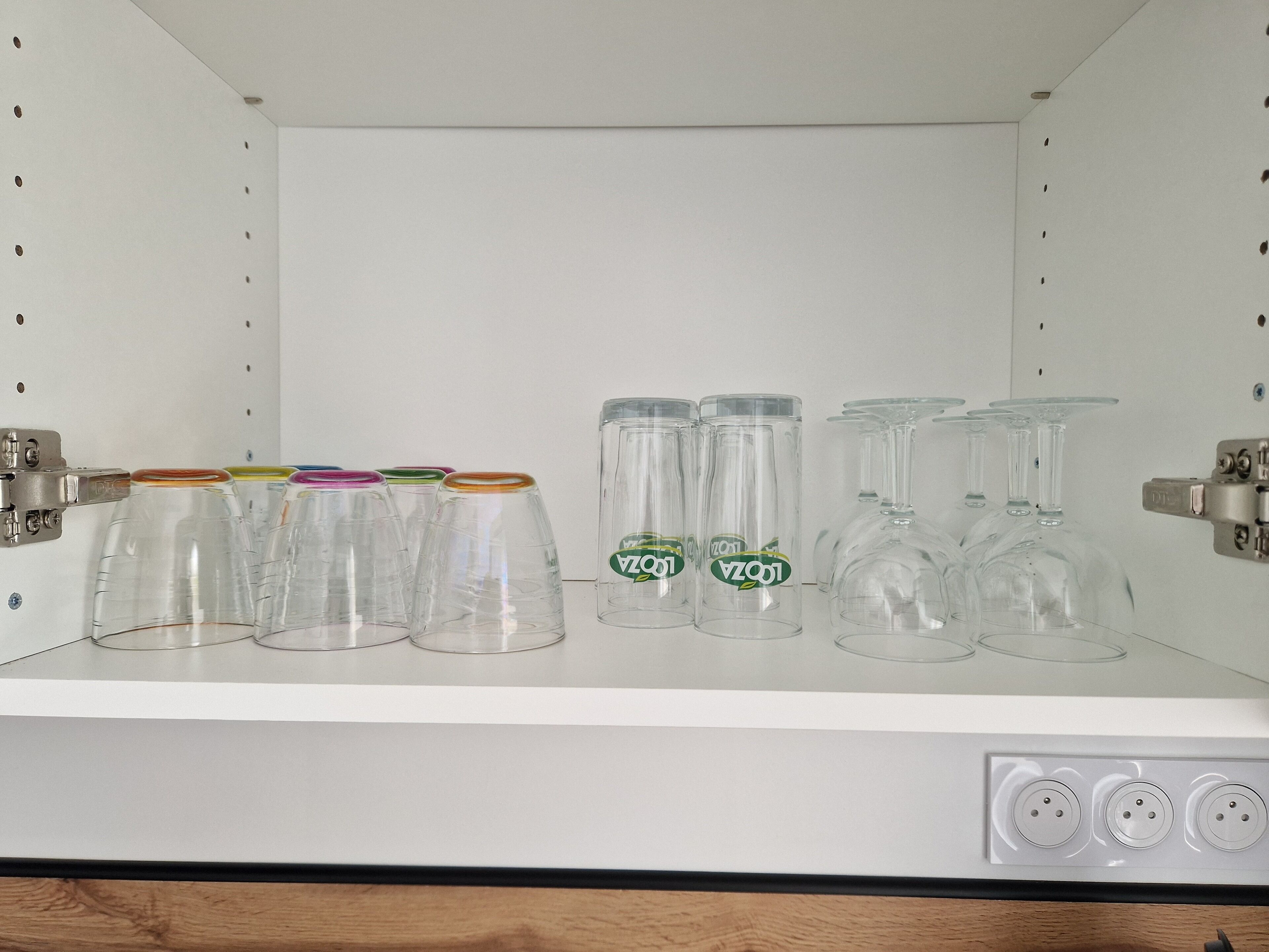 A shelf with various glassware, including wine glasses and tumblers, arranged neatly.