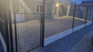 Een omheind buitengebied met een grindpad dat naar de ingang van een gebouw leidt.