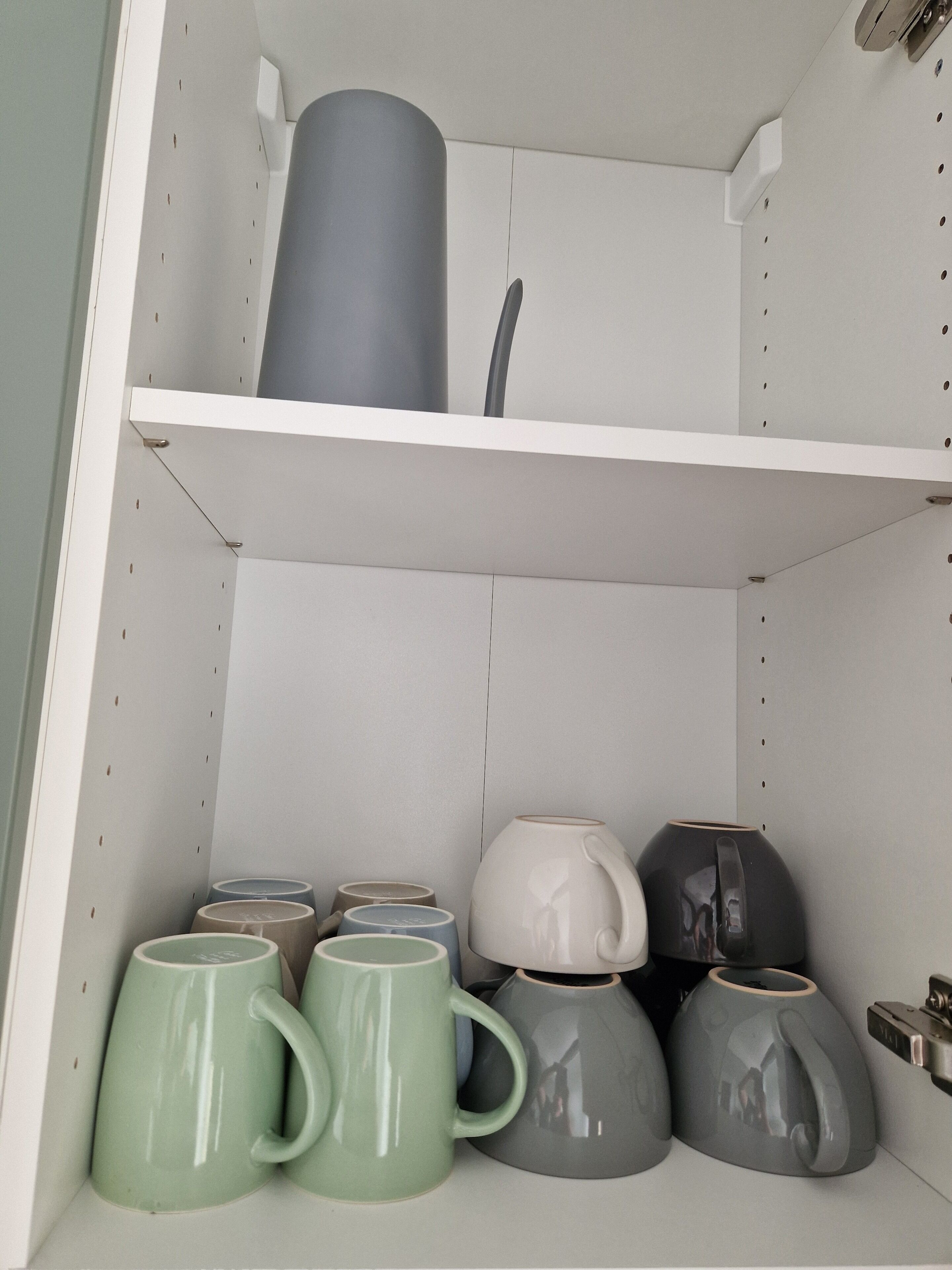 A shelf with various ceramic mugs and a large vase.