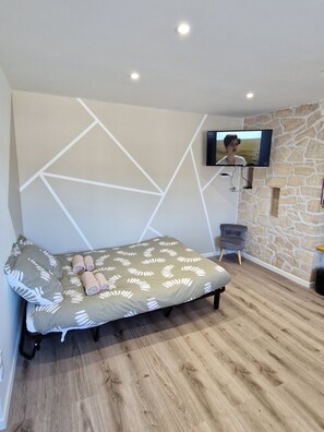 Ein Schlafzimmer mit einem Bett, einem an einer Steinwand befestigten Fernseher und einem Holzboden.