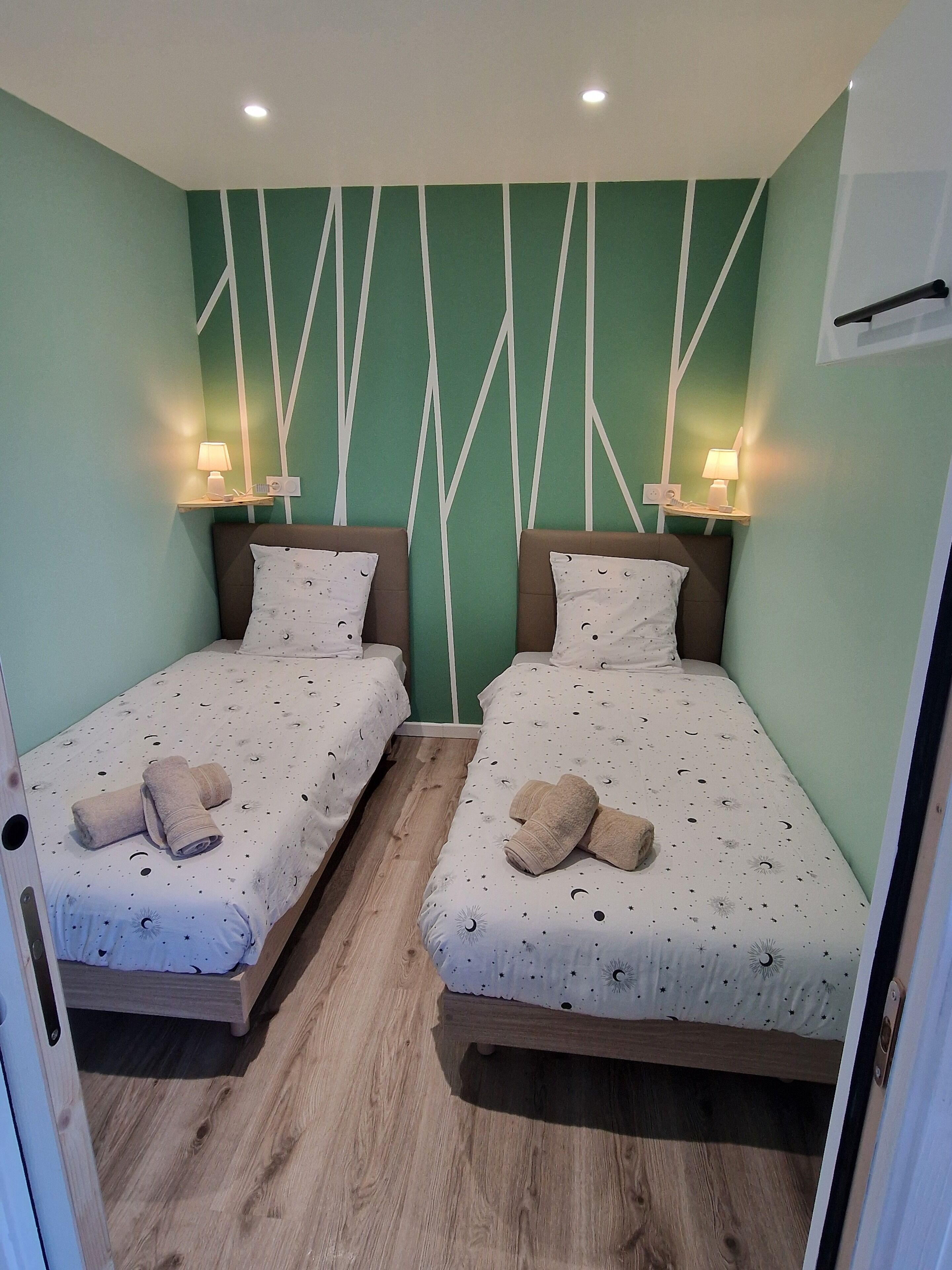 Een tweepersoonskamer met twee bedden, elk voorzien van een nachtkastje en lamp, en een groene wand met een wit patroon.