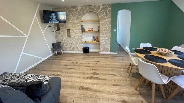 Een moderne woonkamer met een accentmuur van steen, een televisie, een eetgedeelte met een ronde tafel en stoelen, en een trap naar een hoger gelegen verdieping.