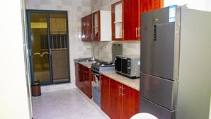 A kitchen with wooden cabinets, a stainless steel refrigerator, a microwave, a stove, and a sink. - Mvita Heights Retreat (Dar es Salaam)