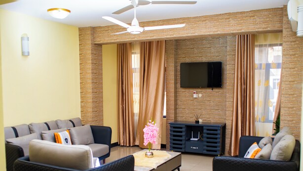 A modern living room with a sofa set, a coffee table, and a flat-screen TV mounted on the brick wall. - Mvita Heights Retreat (Dar es Salaam)
