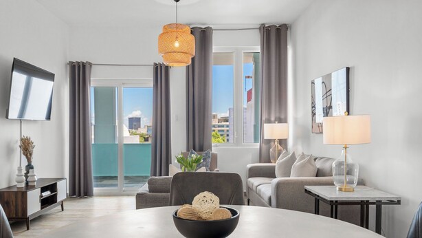 En moderne stue med et rundt bord, en sofa, et fjernsyn og en balkon med gardiner.