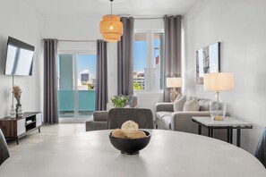 A modern living room with a round table, a sofa, a TV, and a balcony with curtains. - Urban Hideaway | Sleek and Contemporary Unit (San Juan)