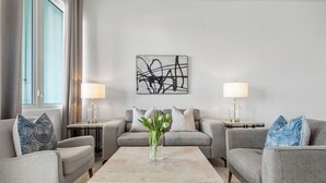 En moderne stue med to grå sofaer, et sofabord i midten, og en vase med blomster. Der er to lamper på sengeborde, og et kunstværk hænger over sofaen.