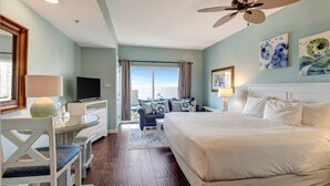 A hotel room with a bed, a desk with a lamp, a television, and a view of the ocean. - Serene Gulf Views: 2-Bedroom 2-Bathroom Retreat at Luau, Panoramic Gulf Views at Sandestin Golf and Beach Resort! (Miramar Beach)