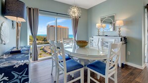 A dining area with a round glass table, white chairs, and a view of the cityscape through large windows. - Serene Gulf Views: 2-Bedroom 2-Bathroom Retreat at Luau, Panoramic Gulf Views at Sandestin Golf and Beach Resort! (Miramar Beach)