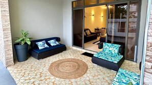 Un espace extérieur abrité, aménagé avec des sièges, un sol décoré, une plante en pot et un canapé avec des coussins.