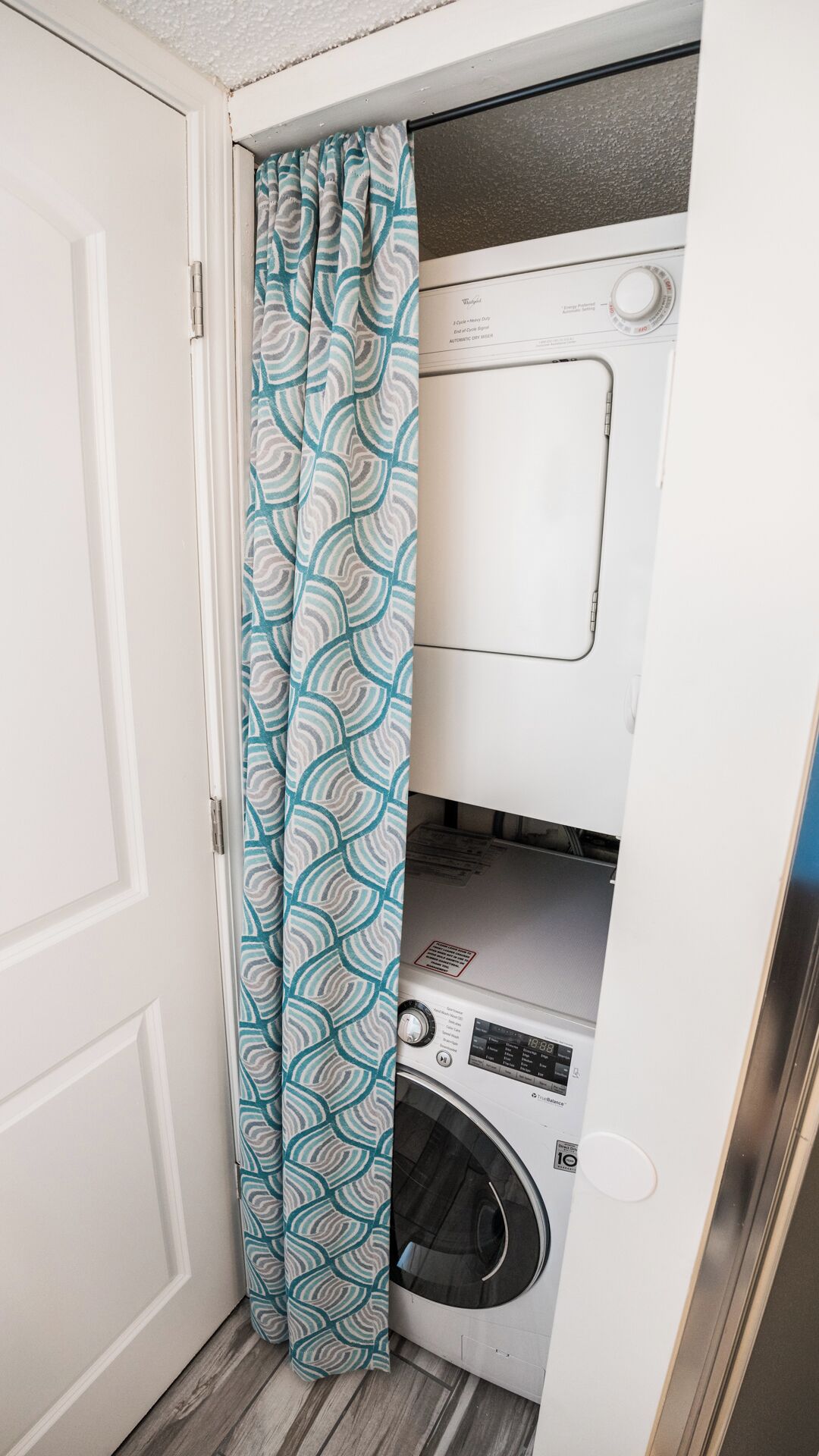 A compact laundry room with a washing machine and dryer, a patterned curtain, and a white door.