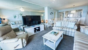 Un salón moderno con un televisor de pantalla plana, un sofá color beige, un sofá a rayas y una mesa de centro.