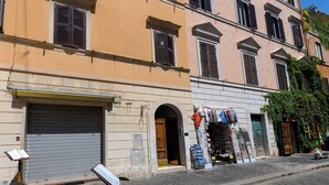 Un immeuble à plusieurs étages avec une porte de garage fermée, un magasin dont les articles sont exposés à l’extérieur, et un scooter garé dans la rue.